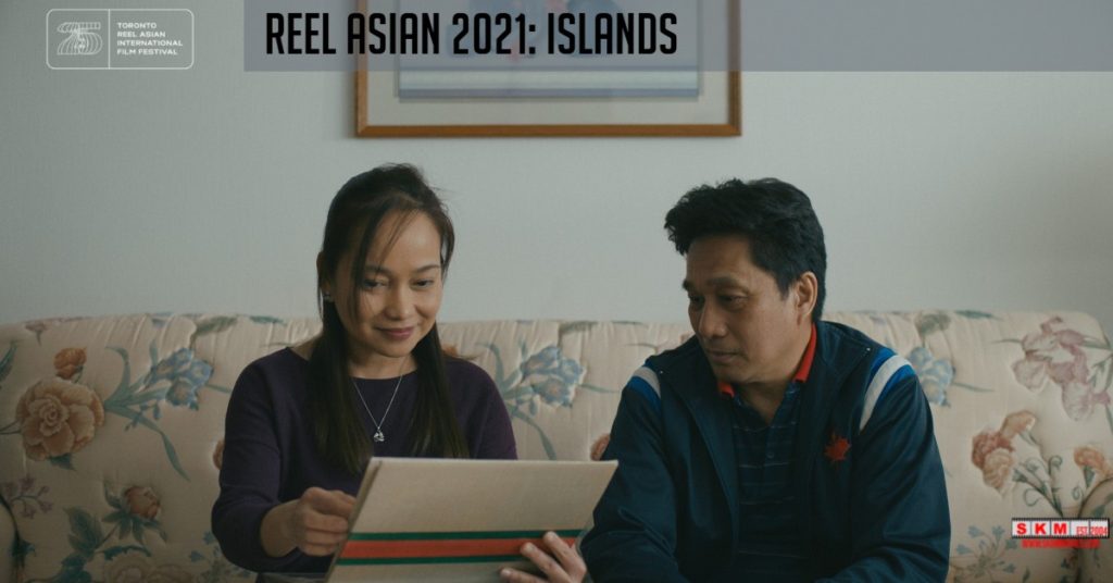 A film still from Islands of two people on a living room sofa looking through an album of old family photographs. Both have black hair and tan skin.